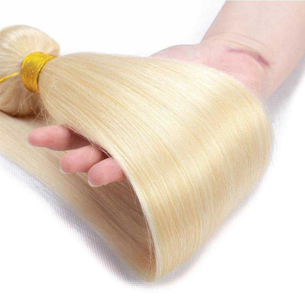 Blonde hair extensions held by a hand on a white background